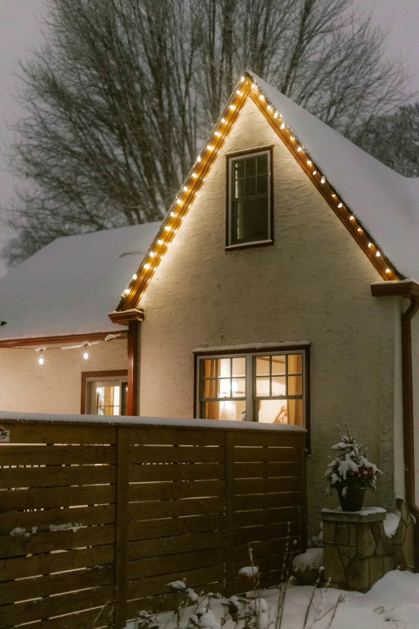 Warm white holiday lights along the roofline of a snow-covered home
