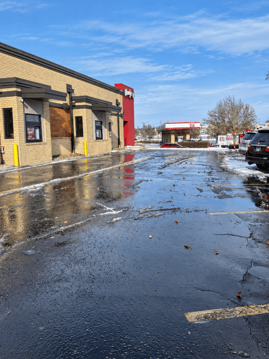 Cleared parking lot beside a restaurant with snow along the pavement edges
