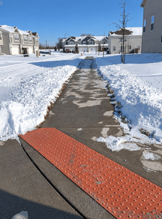 Cleared sidewalk and curb ramp bordered by snow at a multifamily property