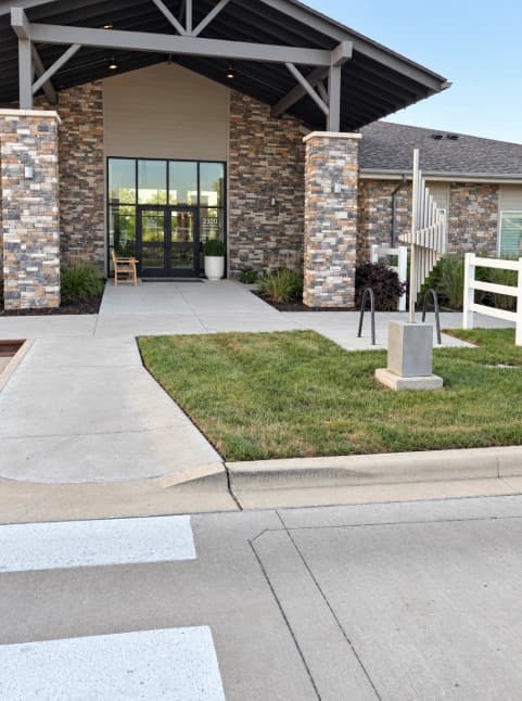 Lawn beside a curved sidewalk leading to a stone-clad building entrance