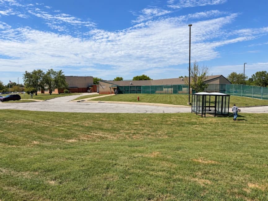 Worker maintaining a lawn beside a shelter, paved drive, and fenced grounds