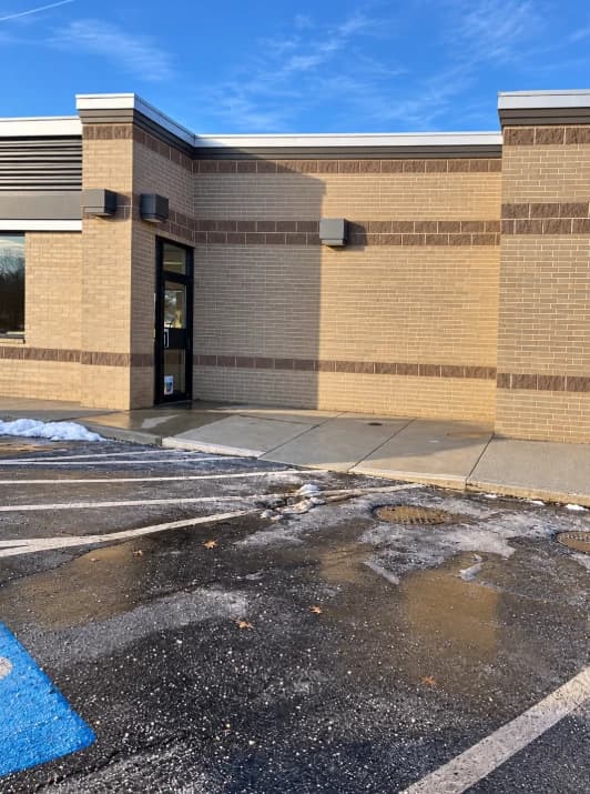 Cleared sidewalk outside a brick building with snow and ice remaining in the adjacent parking area