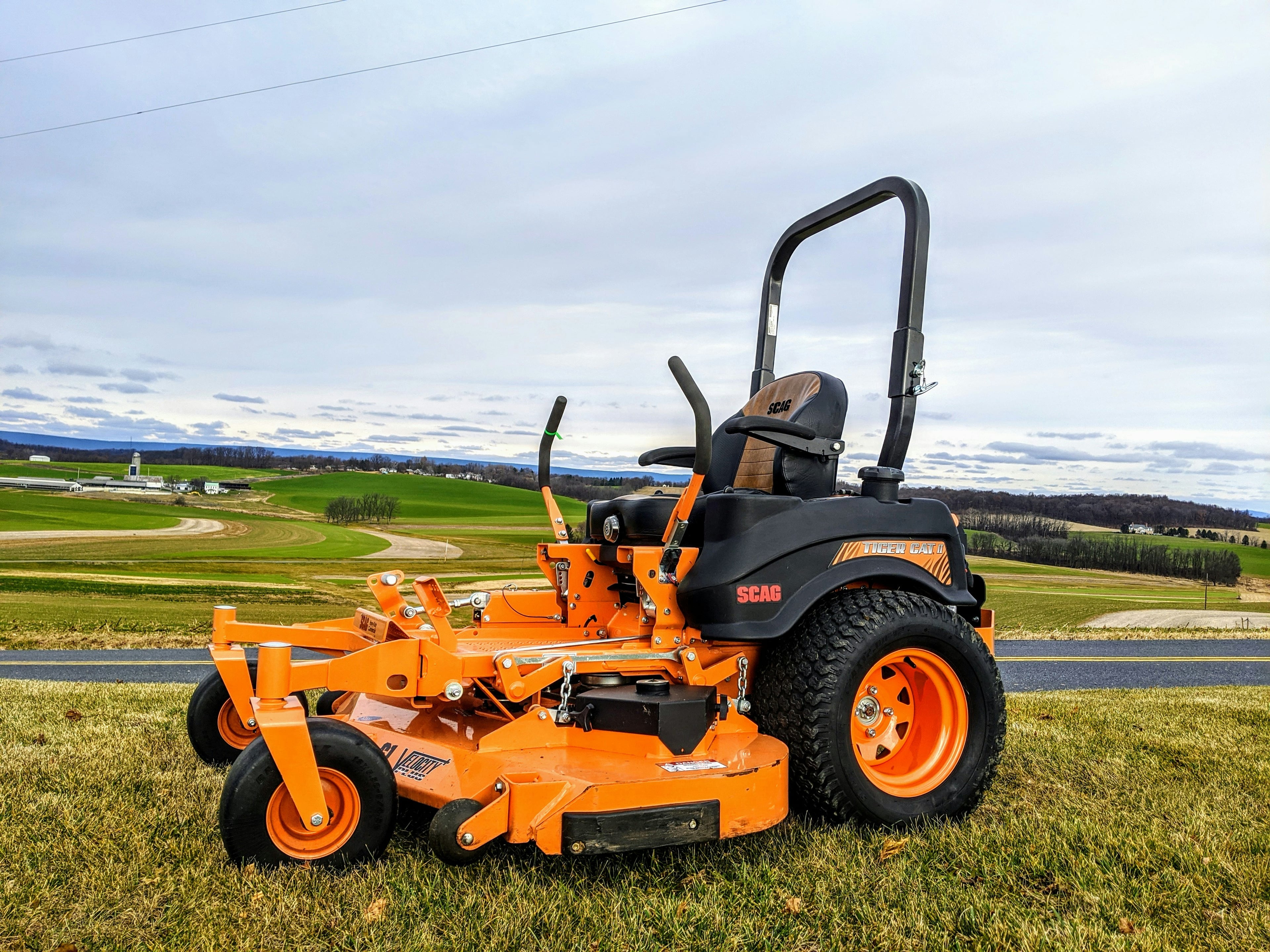 An orange zero-turn mower on grass with rolling green fields in the background