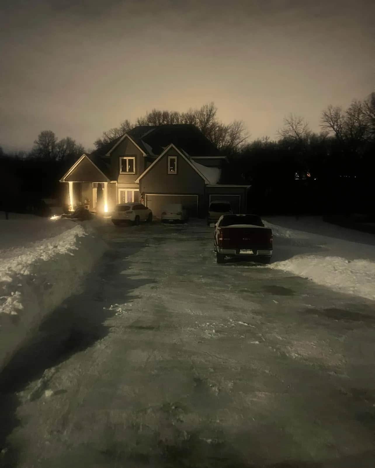Snow-covered driveway in front of a home at night